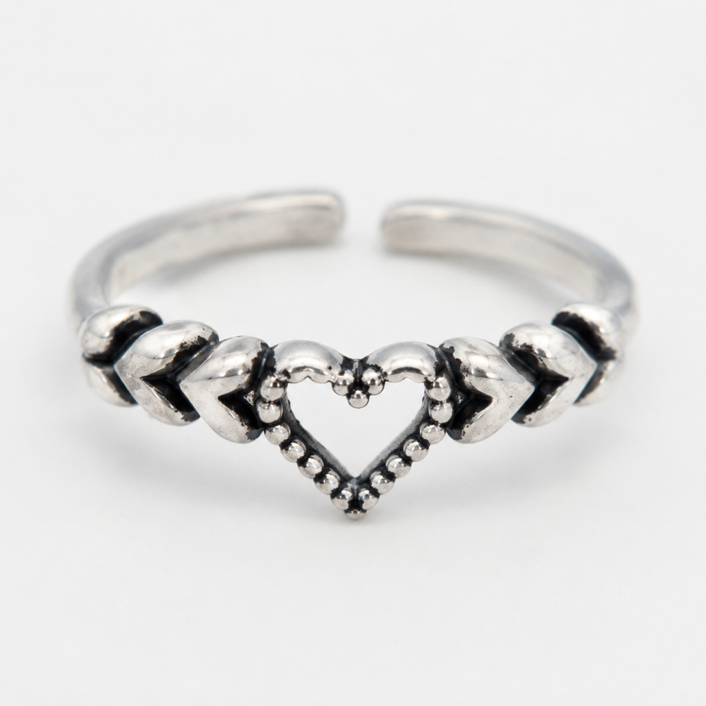 A close up of silver-toned toe ring featuring a central open heart design with textured chevron details on either side, photographed on a clean white background.
