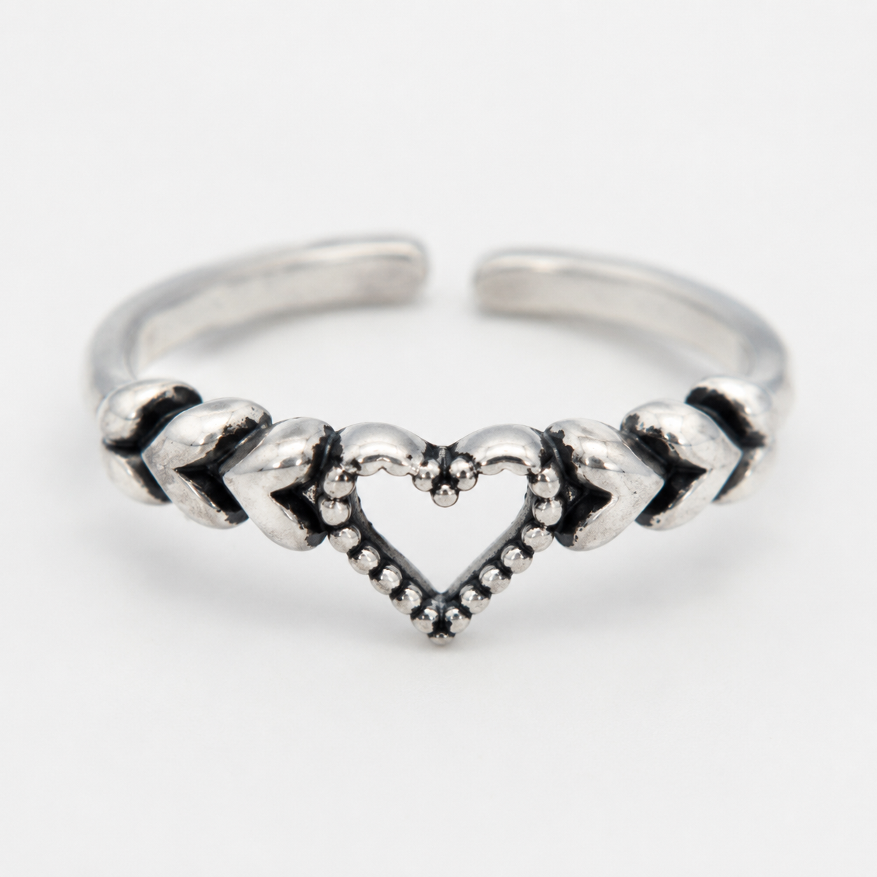 A close up of silver-toned toe ring featuring a central open heart design with textured chevron details on either side, photographed on a clean white background.