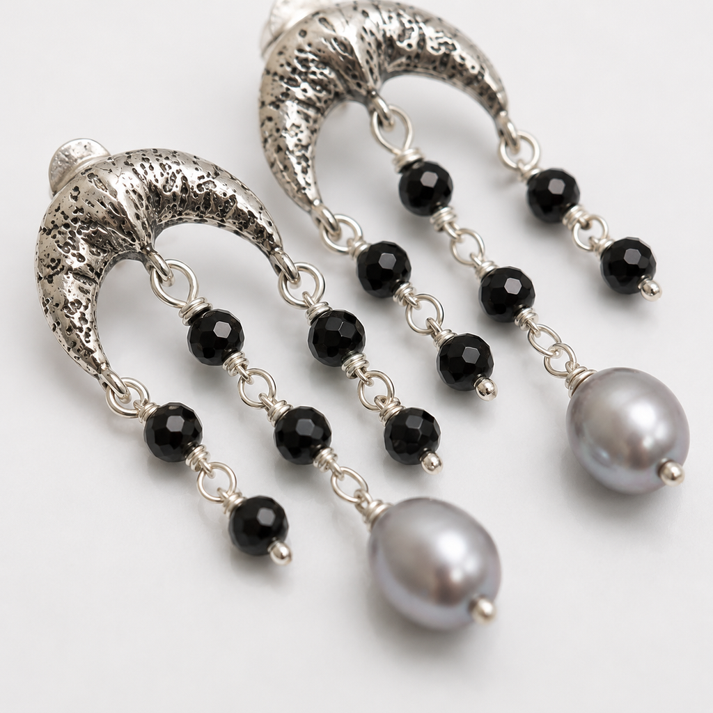 A pair of silver crescent-shaped dangle earrings with faceted black beads and large gray pearl-like drops, photographed on a clean white background.