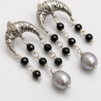 A pair of silver crescent-shaped dangle earrings with faceted black beads and large gray pearl-like drops, photographed on a clean white background.