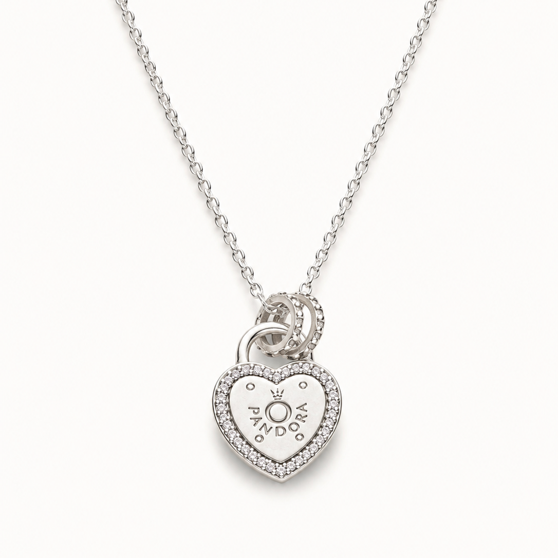 A silver heart-shaped pendant necklace with a small heart and sun motif in the center, surrounded by a border of tiny clear stones, hanging from a delicate silver chain against a light off-white background.