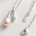 Silver pendant necklace featuring a light pink freshwater pearl and a small crystal-accented charm, displayed on a clean white surface with close-up views of the clasp and chain.