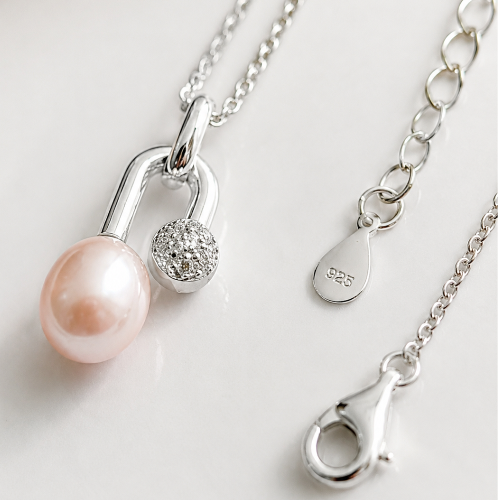 Silver pendant necklace featuring a light pink freshwater pearl and a small crystal-accented charm, displayed on a clean white surface with close-up views of the clasp and chain.