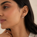 A close-up of a woman wearing a small silver hoop earring with a white pearl at the center, shown against a warm beige background.