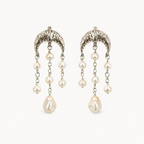 A pair of silver-toned dangle earrings with textured crescent-shaped tops, small pearl-like beads on chains, and larger teardrop pearl drops, shown on a plain light background.