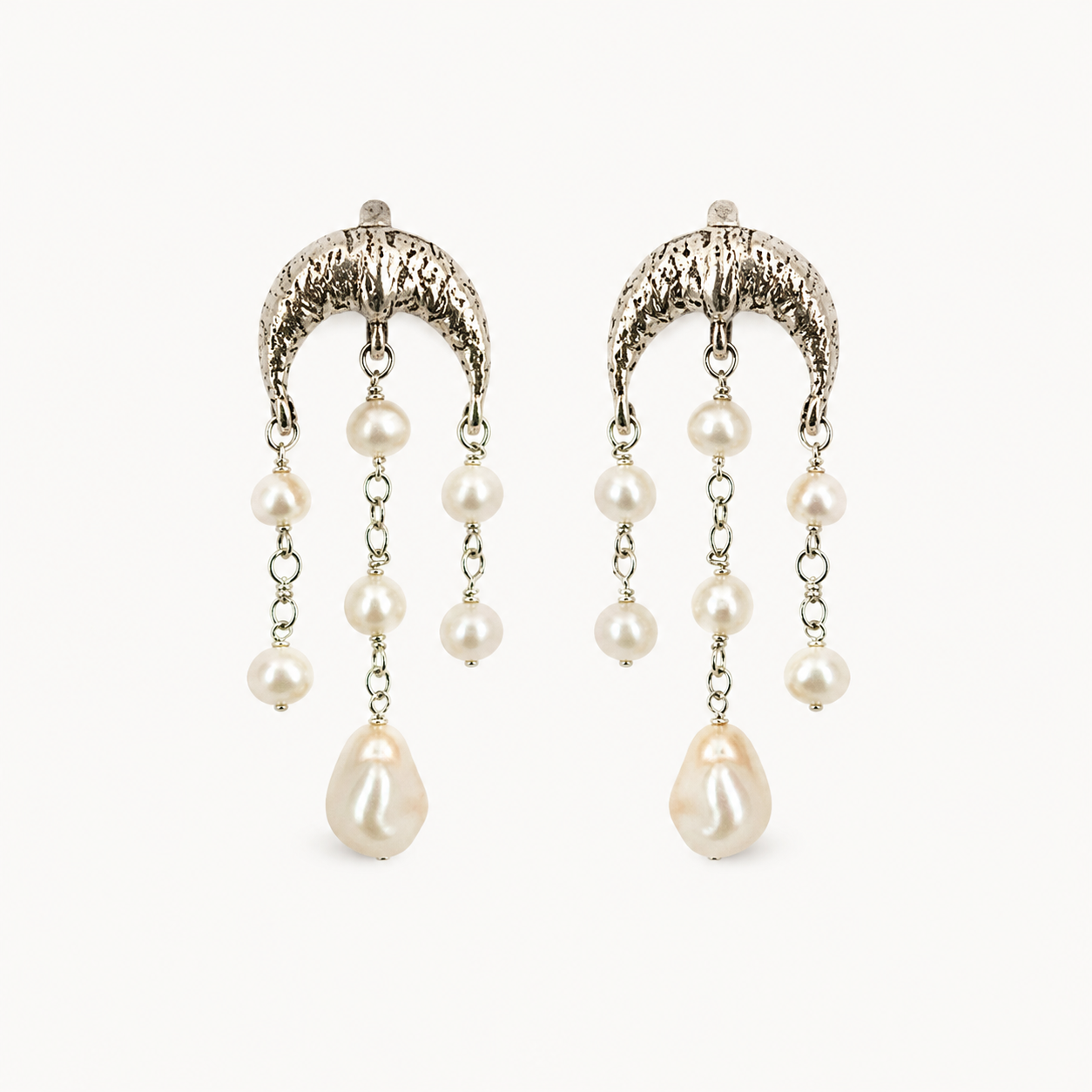 A pair of silver-toned dangle earrings with textured crescent-shaped tops, small pearl-like beads on chains, and larger teardrop pearl drops, shown on a plain light background.