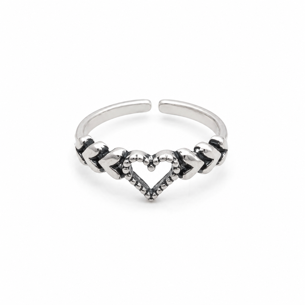 A silver adjustable toe ring featuring a central heart design with textured details and small dark accents, set against a plain white background.