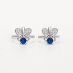 A pair of silver-tone toe rings featuring a butterfly design with pavé-set clear stones and a central round blue gemstone, shown on a plain light background.