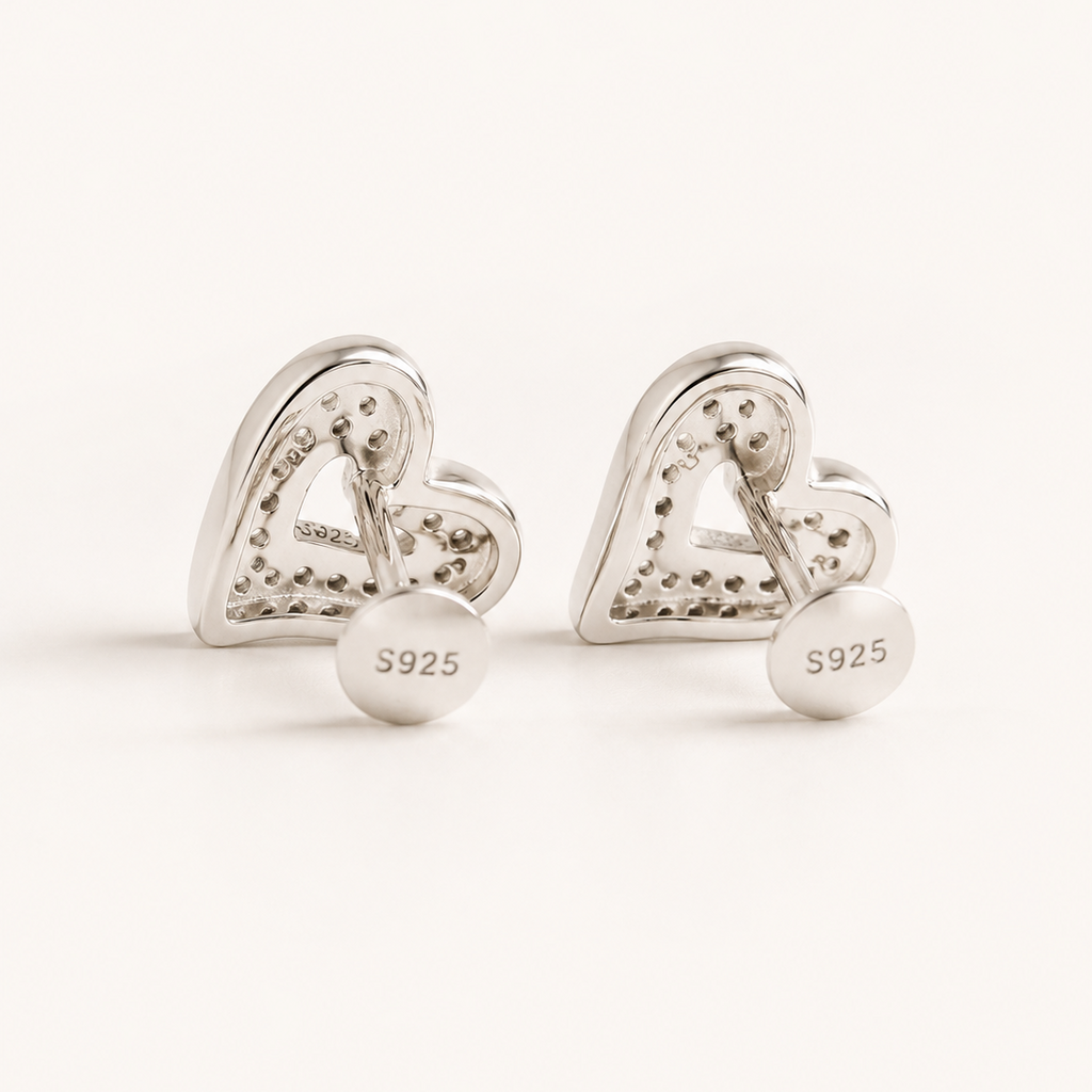 A pair of silver heart-shaped stud earrings with a textured, pave-like surface and a round disc back engraved with 'S925', shown on a clean white background.