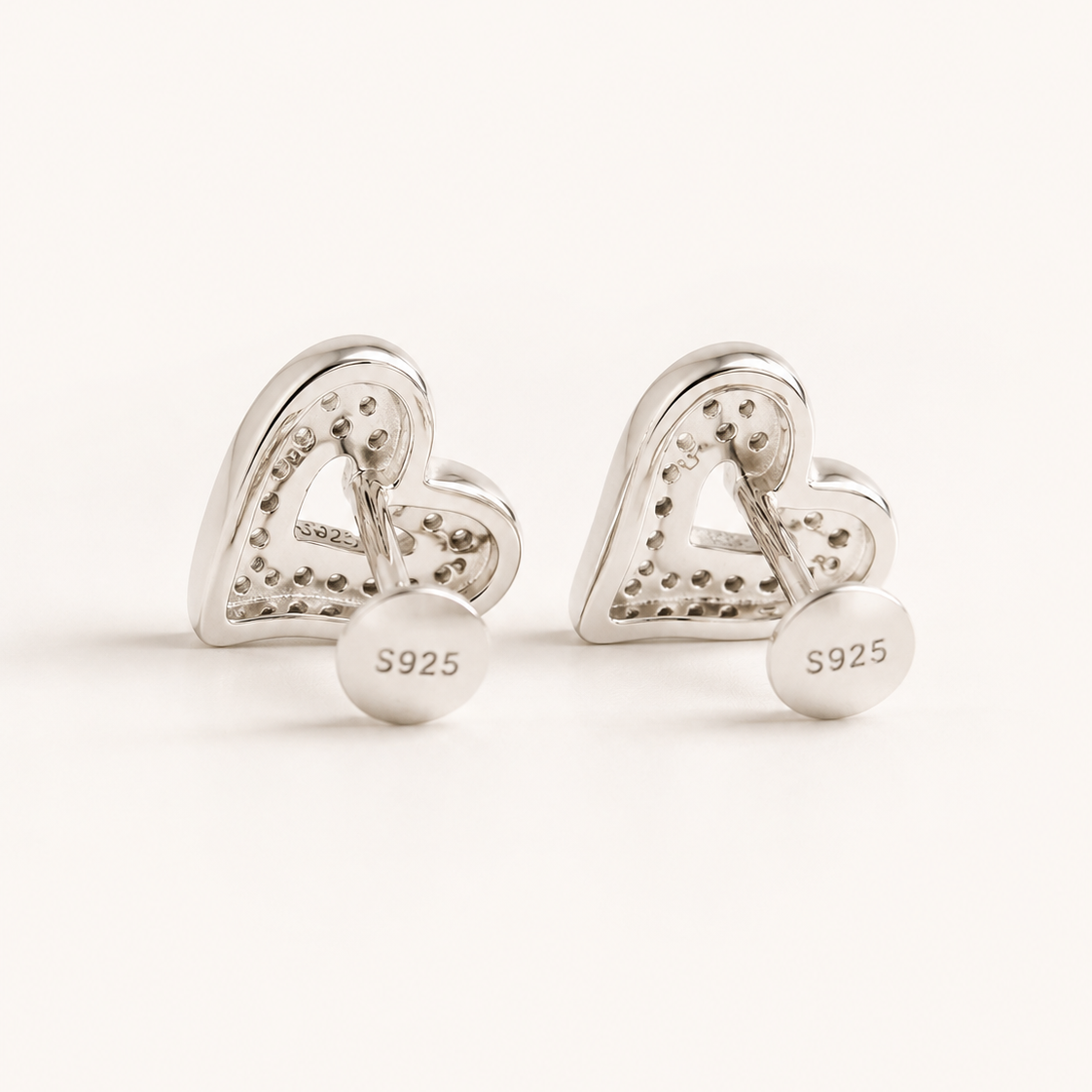 A pair of silver heart-shaped stud earrings with a textured, pave-like surface and a round disc back engraved with 'S925', shown on a clean white background.