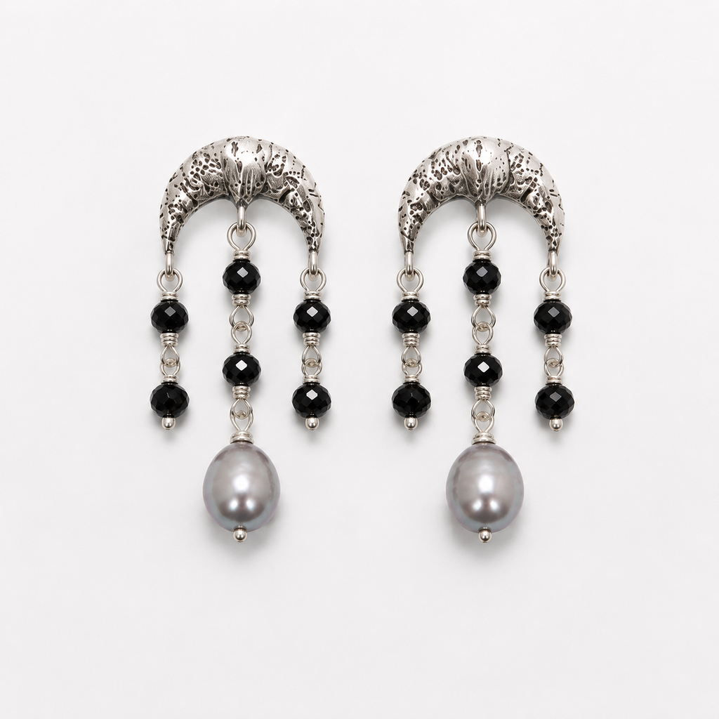 A pair of silver crescent-shaped dangle earrings with black faceted beads, clear spacer beads, and a large gray pearl at the bottom, shown on a light gray background.