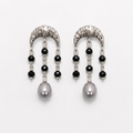 A pair of silver crescent-shaped dangle earrings with black faceted beads, clear spacer beads, and a large gray pearl at the bottom, shown on a light gray background.
