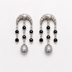 A pair of silver crescent-shaped dangle earrings with black faceted beads, clear spacer beads, and a large gray pearl at the bottom, shown on a light gray background.