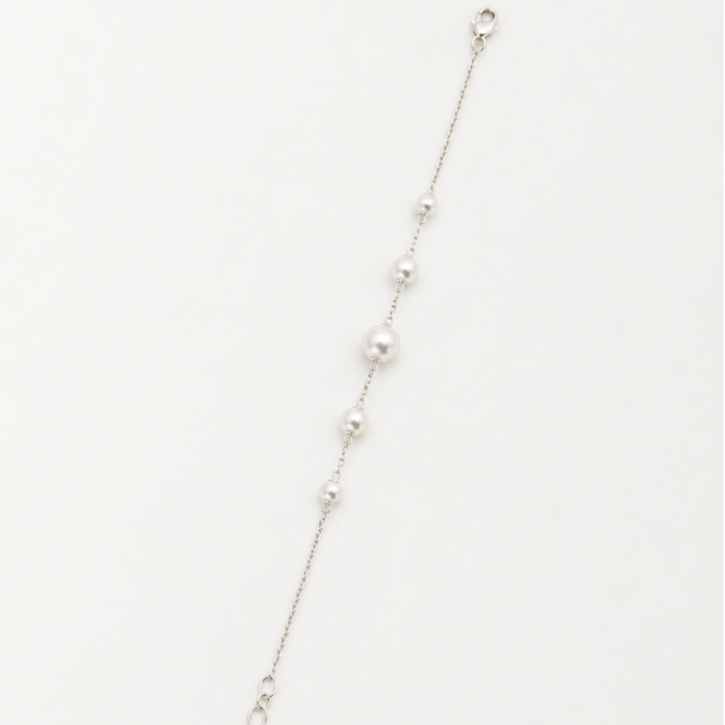 A delicate silver chain bracelet featuring a graduated sequence of white pearls, displayed diagonally on a clean white background.