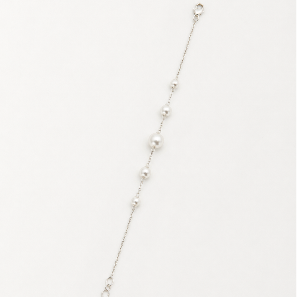 A delicate silver chain bracelet featuring a graduated sequence of white pearls, displayed diagonally on a clean white background.