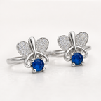A pair of silver butterfly-shaped toe rings with pavé-set heart wings and a round blue gemstone at the center, shown on a clean white background.