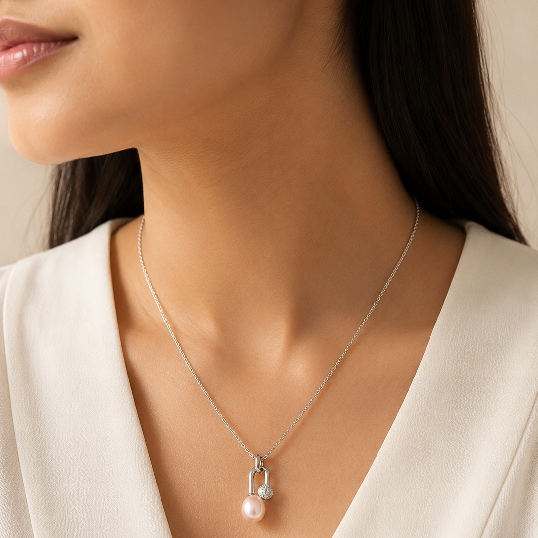 A close-up of a model wearing a delicate silver necklace with a small white pearl pendant and a tiny clear gemstone accent, paired with a white V-neck top.