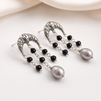 A pair of silver-toned dangle earrings with textured crescent-shaped tops, small black faceted beads, and a large gray pearl drop, photographed on a soft white background.