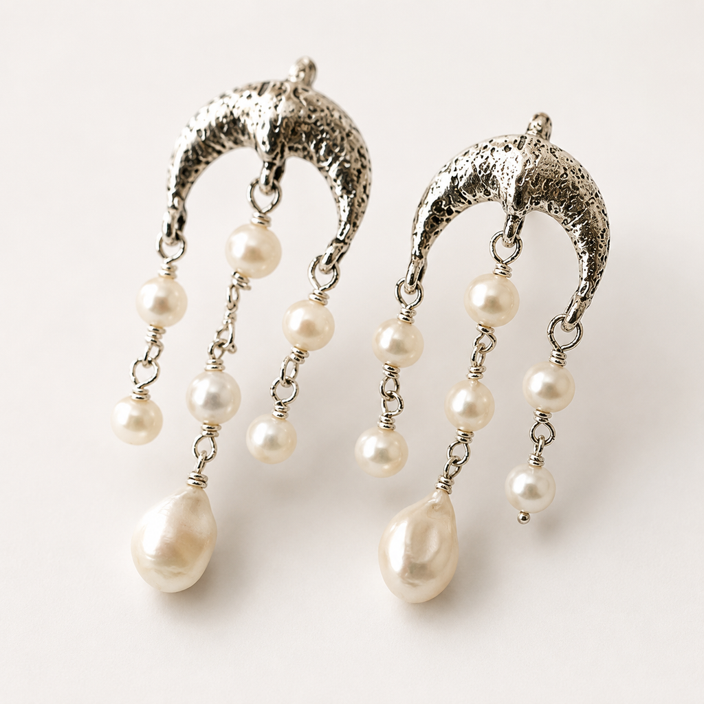 A pair of silver crescent-shaped dangle earrings with textured metal tops and multiple dangling white pearl beads, shown on a plain light background.