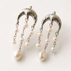 A pair of silver crescent-shaped dangle earrings with textured metal tops and multiple dangling white pearl beads, shown on a plain light background.