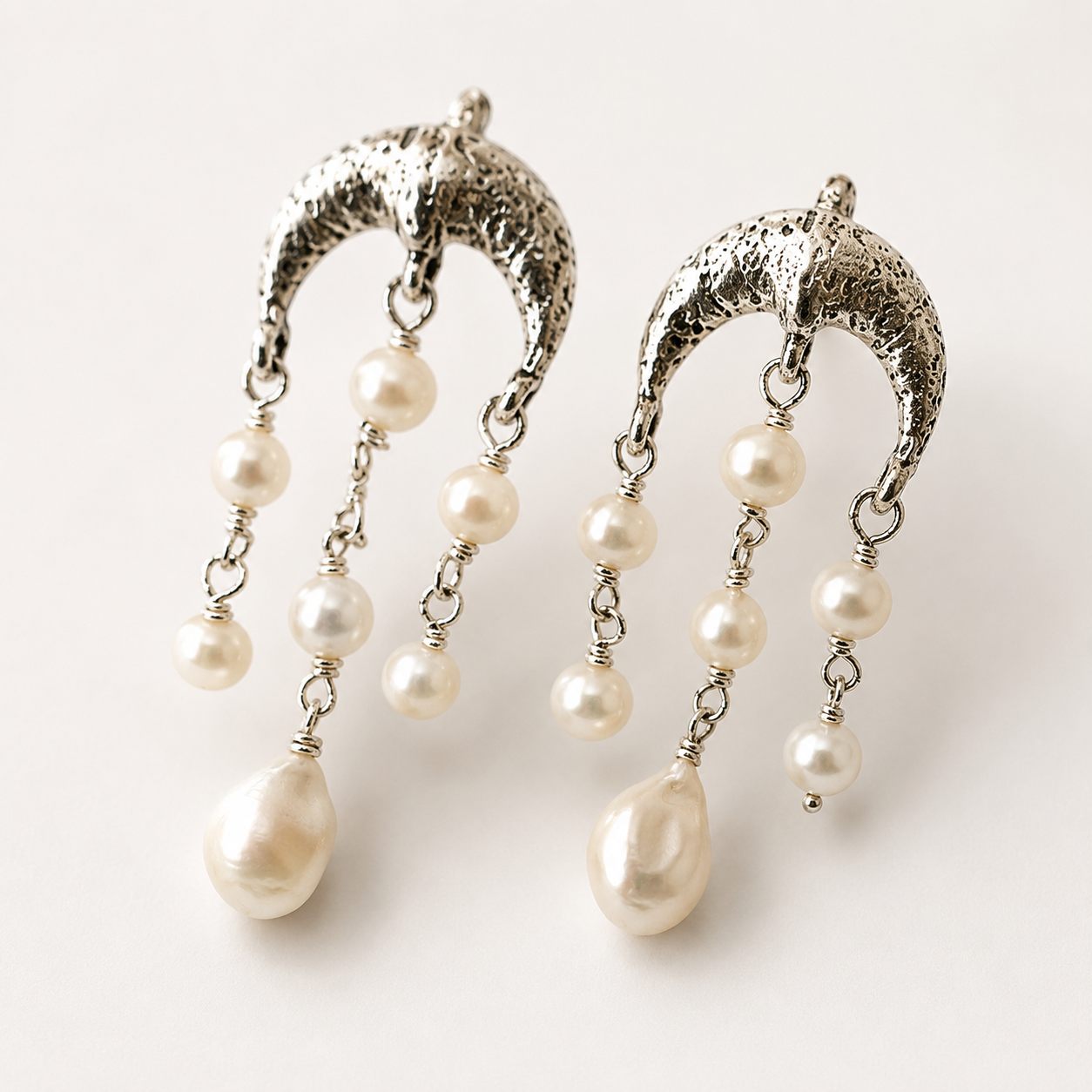 A pair of silver crescent-shaped dangle earrings with textured metal tops and multiple dangling white pearl beads, shown on a plain light background.