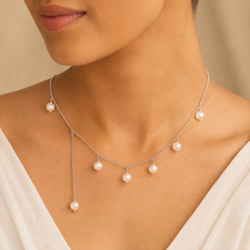 A delicate silver-toned necklace with seven small white pearl drops, shown worn on a model's neck over a white V-neck top.