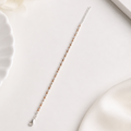 A delicate silver chain bracelet with small rose gold beads, laid diagonally on a clean white surface with soft decorative props.