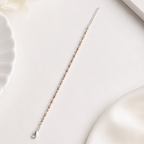 A delicate silver chain bracelet with small rose gold beads, laid diagonally on a clean white surface with soft decorative props.