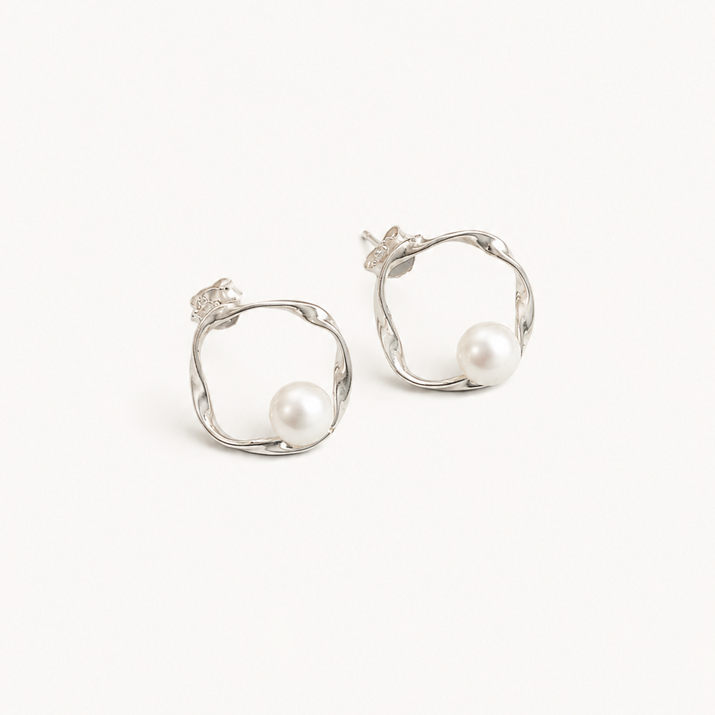 A pair of silver-toned hoop earrings with organic, twisted open-loop shapes and a single white pearl set into each earring, shown on a plain off-white background.