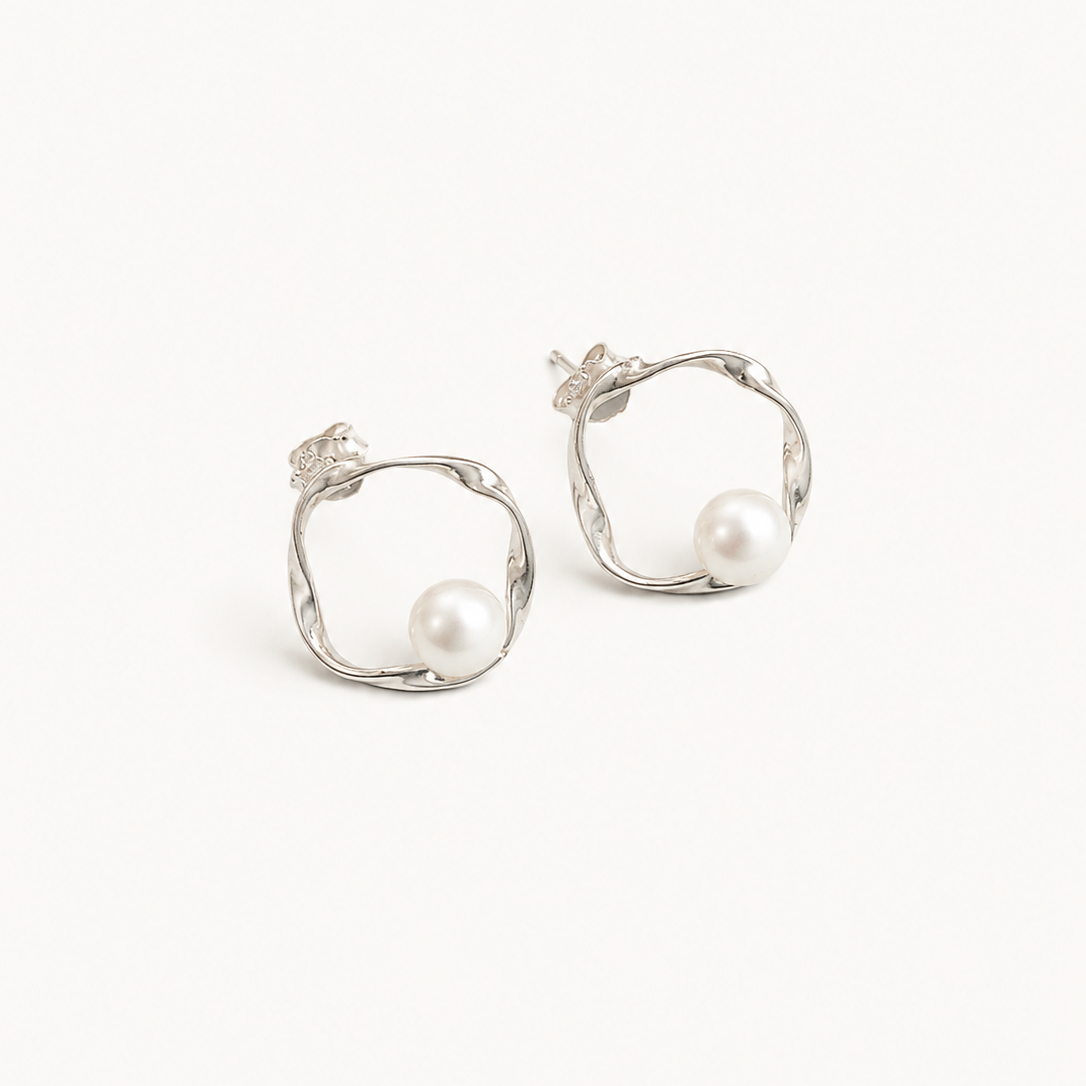 A pair of silver-toned hoop earrings with organic, twisted open-loop shapes and a single white pearl set into each earring, shown on a plain off-white background.