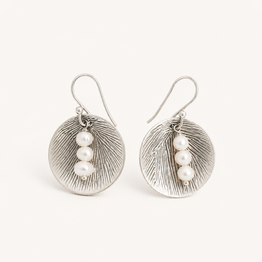 A pair of silver-toned drop earrings with textured oval discs and three small white pearl beads on each earring, shown against a plain off-white background.
