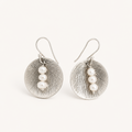 A pair of silver-toned drop earrings with textured oval discs and three small white pearl beads on each earring, shown against a plain off-white background.