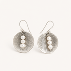 A pair of silver-toned drop earrings with textured oval discs and three small white pearl beads on each earring, shown against a plain off-white background.