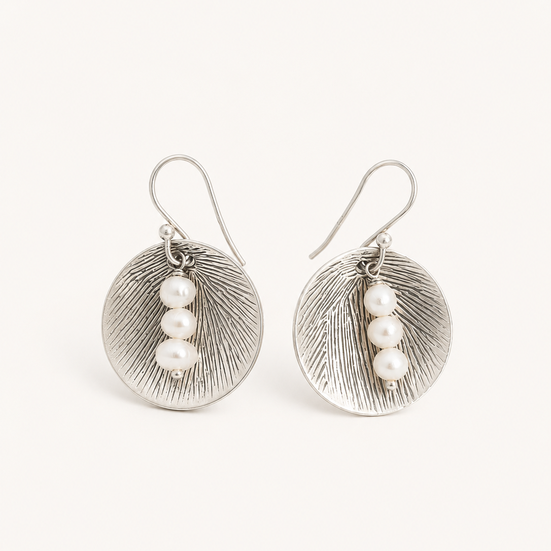 A pair of silver-toned drop earrings with textured oval discs and three small white pearl beads on each earring, shown against a plain off-white background.