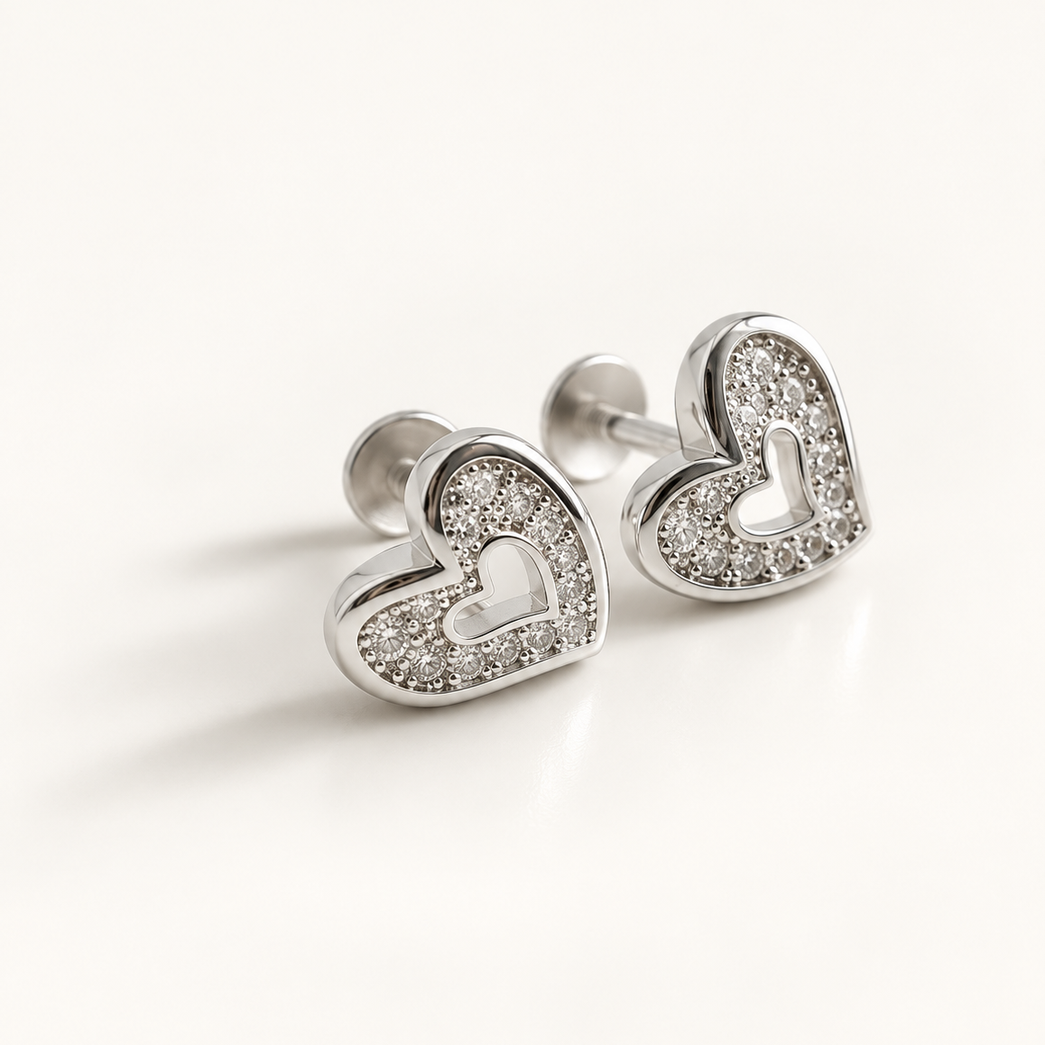 A pair of silver heart-shaped stud earrings with pavé-set clear stones, shown on a clean white background.