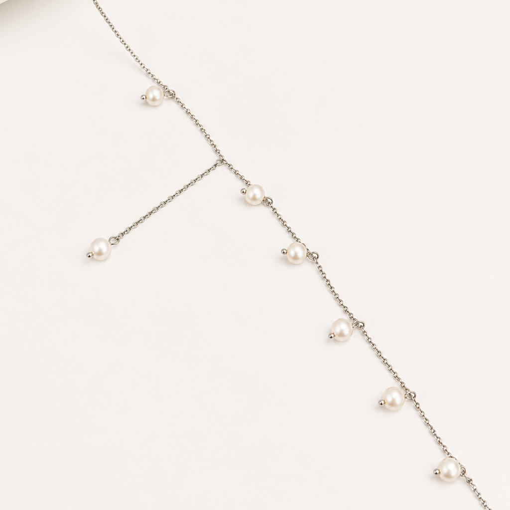 A delicate silver-toned chain necklace with multiple small white freshwater pearls spaced along the chain, displayed on a clean off-white background.
