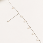 A delicate silver-toned chain necklace with multiple small white freshwater pearls spaced along the chain, displayed on a clean off-white background.