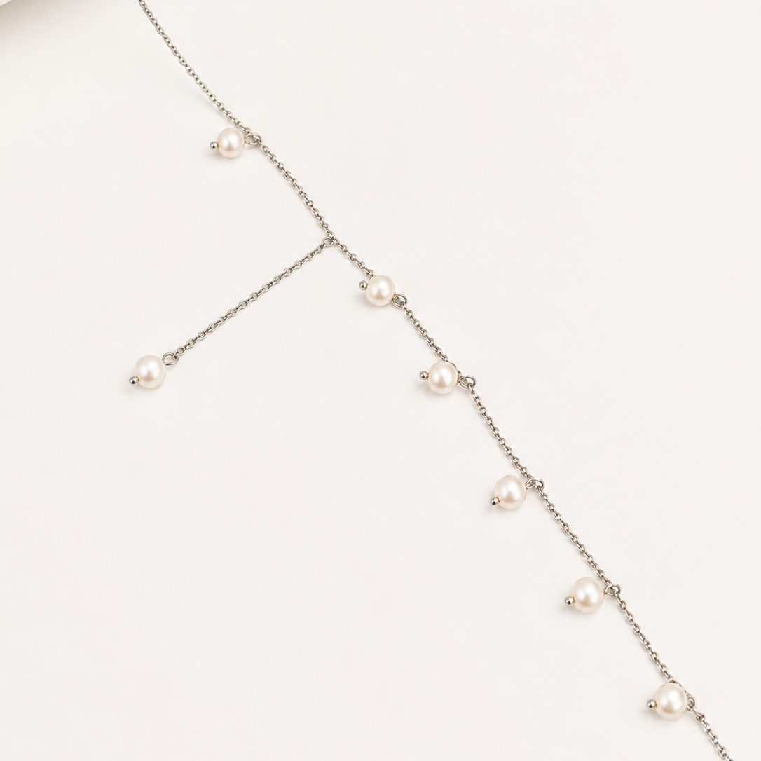 A delicate silver-toned chain necklace with multiple small white freshwater pearls spaced along the chain, displayed on a clean off-white background.