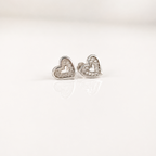 A pair of silver heart stud earrings with clear crystal accents, displayed on a clean white reflective surface.